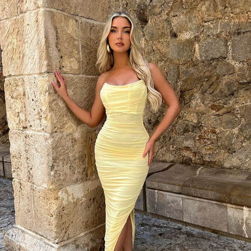 Model is wearing a strapless yellow mesh midi dress with corset boning and a thigh high slit. The strapless midi dress is ruched and is a bodycon style. 