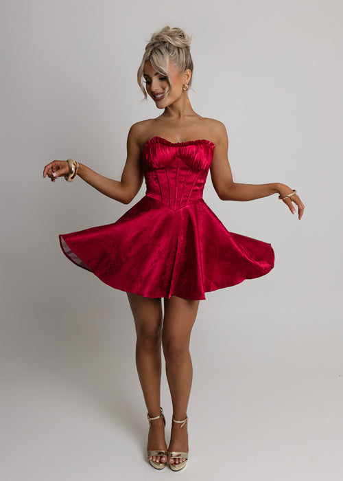 Women's red satin strapless mini dress with corset style bodice and floaty fit. Model is 5ft2' and wears a size XS.