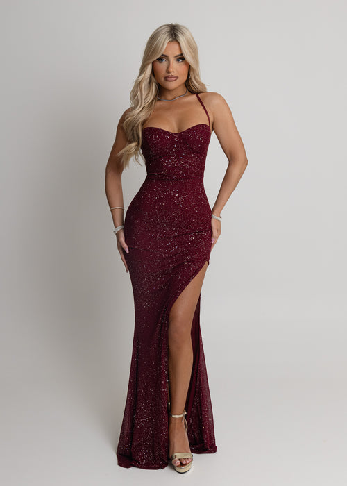 Women's burgundy maxi dress crafted with sparkle mesh fabric, thigh high slit and adjustable straps. Figure hugging fit and halter neckline.