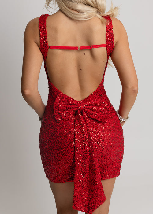 Women's red sequin mini dress with bodycon fit, open back and embellished sequin bow design on low back. Model is 5ft2' and wears a size XS 6.