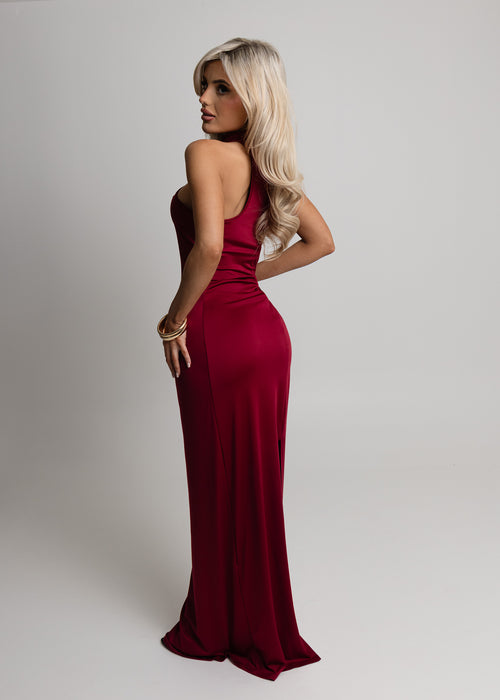Back image of woman standing up against a white backdrop wearing wine colour maxi dress with racer style back and figure-hugging fit.