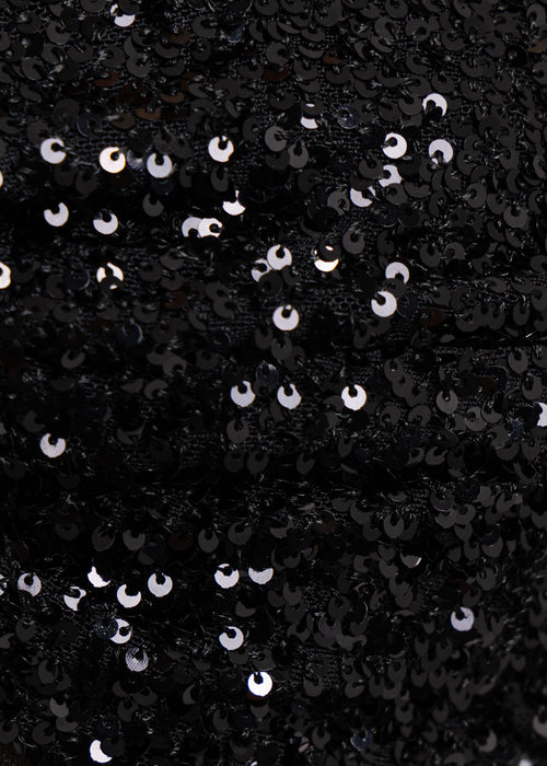 Close up swatch of fabric showing black shiny sequin embellishments sewn into the romper.