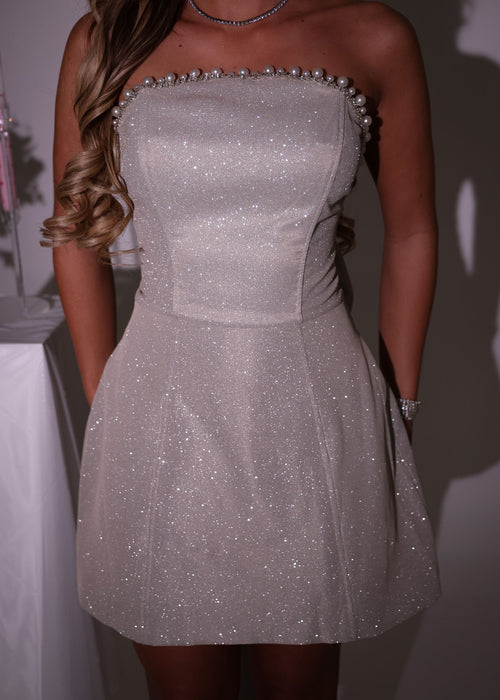 Women's champagne glitter mini dress with large detachable bow on the back of mini dress. Pearl and diamante trim embellishments with a strapless fit. Model is 5ft2' and wears a size XS 6.