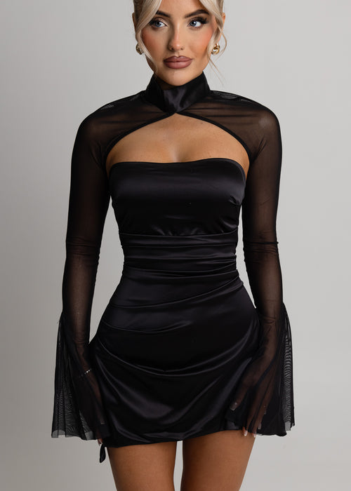 Women's black satin mini dress with long mesh sleeves which flare at the wrist. Model is 5ft2' and wears a size XS.