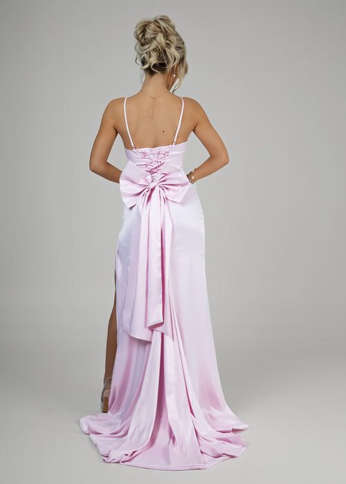 Women's pink satin gown back view with tie up back, adjustable straps and large bow detail on bottom waist of gown.